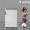 A white Bomann refrigerator is shown in front of a gray brick wall and a wooden floor. Circular images showing berries, vegetables, meat, and a glass of water are displayed to the right of the refrigerator, with the text "IDEAL FÜR" above them. Voir les images du produit