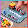A child's hand is building with LEGO-style blocks on a blue baseplate. A storage container filled with blocks is visible in the foreground. Produktbild-Vorschau