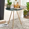A small round side table with a green marble top and gold legs, placed on a fluffy rug next to a window. It is decorated with plants and a carafe with glasses. Produktbild-Vorschau
