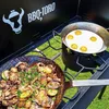 A BBQ-Toro gas grill table with a wind guard, a cast iron gas stove with two burners, and food being cooked on the stove. Produktbild-Vorschau