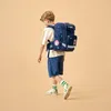 A young boy walks away from the camera, wearing a backpack. Produktbild-Vorschau
