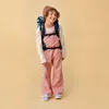 A young child wearing a backpack and overalls, standing against a plain background. Produktbild-Vorschau