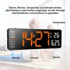 A digital clock displaying time, date, and temperature, with people in the background doing yoga. Produktbild-Vorschau