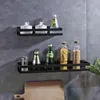 Two black shelves mounted on a gray tiled wall, holding various kitchen items like jars of pasta and spices, and bottles of drinks. Náhled obrázku produktu