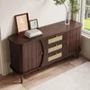 A dark wood sideboard with rattan drawer fronts and sliding doors, decorated with framed pictures and books, placed in a room with natural light coming from a window. Podgląd zdjęcia produktu