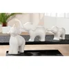 Three white ceramic elephant figurines arranged in a line on a dark surface. Produktbild-Vorschau