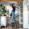 A woman is decorating a hallway with a string of paper stars, standing on a stepladder. Podgląd zdjęcia produktu