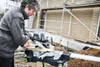 A man is using a miter saw to cut wood at a construction site. Podgląd zdjęcia produktu