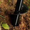 A close-up of a black auger drill bit digging into brown soil. Podgląd zdjęcia produktu