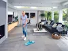 A woman is mopping the floor in a modern living room with large windows. Produktbild-Vorschau