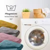 A washing machine with folded blankets in front of it, and a plant and basket on top. Produktbild-Vorschau