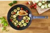 A frying pan with cooked chicken and zucchini, surrounded by fresh ingredients on a wooden table. Voir les images du produit