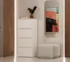 A white chest of drawers with four drawers stands next to a gold-framed mirror in a hallway or entryway. Náhled obrázku produktu