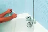 A person is applying sealing tape to the edge of a bathtub. Produktbild-Vorschau