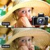 A split image showing a child wearing a large straw hat, with a digital camera in the top panel and text overlays. Produktbild-Vorschau