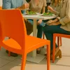 People are sitting at a table outdoors, enjoying drinks and food, with an orange chair prominently in the foreground. Voir les images du produit