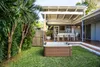 A backyard scene with a hot tub in the foreground and a covered patio with a dining set in the background. Náhled obrázku produktu