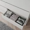 A close-up view of an open drawer in a white dresser, revealing folded t-shirts inside. Náhled obrázku produktu