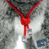 A close-up of a red cord with a knot and two silver decorative elements, attached to a gray furry surface. Produktbild-Vorschau