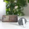 A smartphone displaying a music player is placed on a desk next to a wireless charger and headphones, with a laptop and greenery in the background. Anteprima dell’immagine prodotto