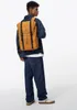 A person wearing a denim jacket and jeans, carrying a yellow backpack. Náhled obrázku produktu