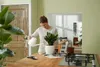 A woman is watering a plant in a pot on a wooden table. Produktbild-Vorschau