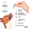 A dog is licking its lips while a hand holds a dried fish treat above it. The image includes text and icons describing the product's features. Produktbild-Vorschau