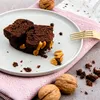 A close-up shot of chocolate cake slices with peanuts on a plate, with walnuts and a napkin in the background. Náhled obrázku produktu
