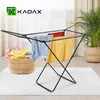 A black KADAX clothes drying rack with laundry hanging on it, placed on a white rug next to a basket of laundry and a potted plant. Podgląd zdjęcia produktu