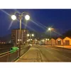 A street scene at dusk with streetlights illuminating the road and sidewalk. Voir les images du produit
