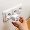A hand is holding a white travel adapter in front of a white electrical outlet. Produktbild-Vorschau