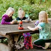 Three young girls are using microscopes at a wooden picnic table outdoors. Produktbild-Vorschau