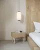 A bedside table with books and a glass next to a bed with a wooden headboard, under a pendant lamp. Produktbild-Vorschau