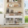 A white buffet sideboard with various kitchen items displayed on it and in its open compartments, set in a well-lit room with a window showing a garden and house. Produktbild-Vorschau