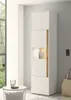 A tall, narrow white cabinet with wood accents and a lit display shelf, placed in a well-lit room next to a window and a small round table. Produktbild-Vorschau
