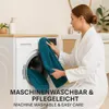 A woman in a white bathrobe is putting a teal towel into a washing machine. Produktbild-Vorschau