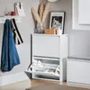 A white shoe cabinet with two flip-down drawers is shown in a hallway setting, with a denim jacket and a striped scarf hanging on a wall rack. Podgląd zdjęcia produktu