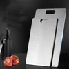 Two stainless steel cutting boards are shown, one behind the other, with a knife block and tomatoes in the background. Produktbild-Vorschau