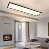 A modern living room with a fireplace, sofa, and coffee tables, illuminated by a large rectangular ceiling light. Podgląd zdjęcia produktu