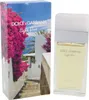 Parfumflakon Dolce & Gabbana Light Blue Escape to Panarea neben Verpackung mit mediterraner Küstenlandschaft, Palmen und pinken Bougainvilleen. Anteprima dell’immagine prodotto