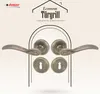 A marketing image showcasing a set of bronze-colored door handles and rosettes, presented within an arched frame against a patterned background. Produktbild-Vorschau
