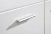 A close-up view of a silver handle on a white cabinet door. Produktbild-Vorschau
