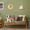 A dog is lying on a sofa in a living room with a clock on the wall. Produktbild-Vorschau