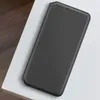 A black leather phone case is placed on a white surface, with a wooden surface visible in the background. Produktbild-Vorschau
