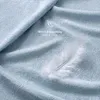 A close-up of a light blue textured fabric, likely a bedsheet, with a single white feather resting on it. Produktbild-Vorschau