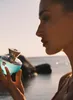 A woman is holding a perfume bottle by the sea. Anteprima dell’immagine prodotto