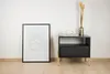 A framed print and a nightstand with a vase and cup are placed against a white wall. Produktbild-Vorschau