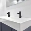 A close-up shot of a modern bathroom sink with two black sensor faucets. Produktbild-Vorschau