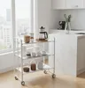 A white three-tier serving cart with various kitchen items on it, placed in a bright kitchen setting with a large window. Voir les images du produit