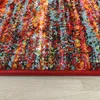 A close-up view of a colorful, textured rug with a red border, resting on a light wooden floor. Produktbild-Vorschau